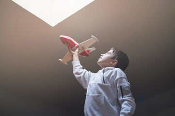 Preteen boy playing with a toy airplane pretending to fly in the attic of his home. Daydreaming concept.