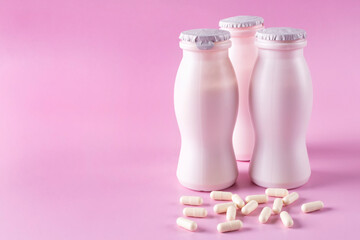 Three bottles of milk yogurt (kefir) and capsules with probiotic on a pink background. The concept of an alternative to pills and a healthy diet. Space for text.