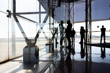 View from inside an airport of silhouettes of unrecognizable people on the facade looking towards...