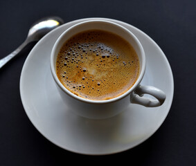 Juicy freshly brewed coffee with foam in a white cup on a black background. Beautiful cup of coffee close-up from above.