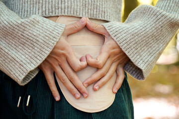 heart-shaped hands on a woman's ostomy in the forest. colostomy bag for colon cancer