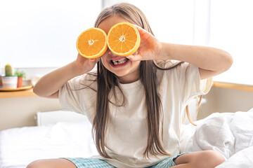 Little girl holding oranges near her eyes while sitting in bed.