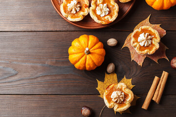 Pumpkin mini pies with whipped cream and spices on a wooden background. copy space