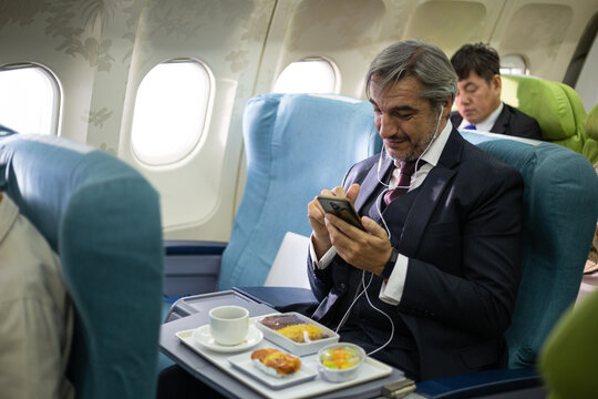 Caucasian businessman using mobile phone working or browsing internet at seat on airplane while eating food on flight. travel airline service, business trip