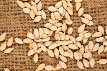 Unpeeled raw pumpkin seeds  on jute cloth, macro, top view.