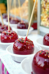 apples glazed in red caramel on wooden stick and sprinkled with multicolored icing sugar, festive sweet treat made of apples