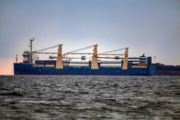 A ship sails on the horizon with windmill blades on board next to another ship	
