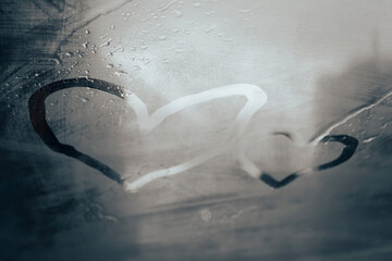 Two heart drawings by finger on steamy window glass with raindrops