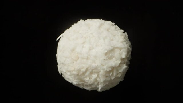 Candy ball with coconut chips. Rotates on a black background, close-up.