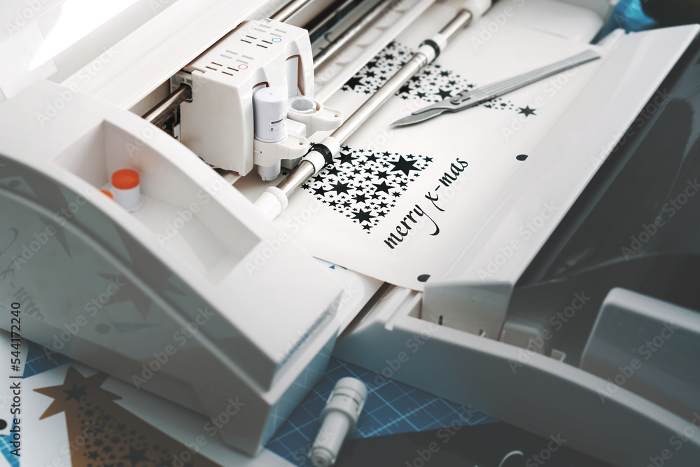 Fototapete plotting machine cuts christmas sticker with stars and lettering from black vinyl. work scene with t