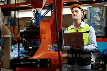 factory worker or engineer holding a laptop computer and controlling robot machine in the factory © offsuperphoto