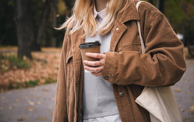 A woman holds a disposable glass of coffee in her hand on a walk in the park.