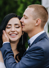 Wedding photo, portrait of a smiling stylish groom in a blue suit and a curly happy brunette bride close-up.