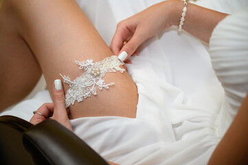 Slender sexy bride puts a garter on her leg close-up. The bride's fees for the wedding. Preparation for the wedding celebration.