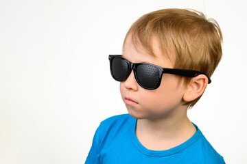 A little boy in black medical glasses for vision correction looks to the left, a place for text