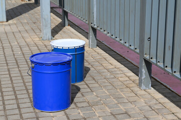 a large blue bucket with white paint stands on the concrete floor on the construction site.