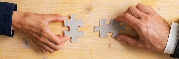 Wide view image of businessman and businesswoman hands merging two blank matching puzzle pieces