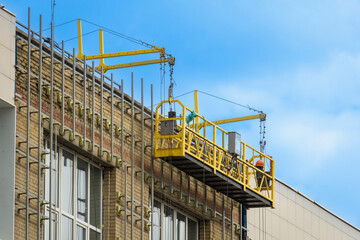 Fototapeta premium Cabin of the front elevator on cables. Facing the facade of the building with tiles. External construction works, equipment.