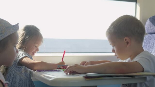 Three little Happy Children are Traveling by train. Small Tourists on vacation, travel around the world. Kid friends are drawing during trip in Summer, dreaming about something.Childhood, Friendship