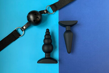 Sex toys, BDSM toys. Black butt plugs and gag on blue background. Useful for adult, sex shop