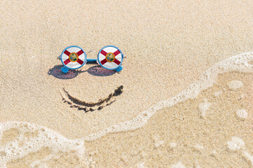 Fototapeta na wymiar A painted smile on the beach and sunglasses with the Florida state flag. The concept of a positive holiday in the resort of Florida.