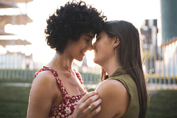 Side view portrait of pretty woman with afro hair and long-haired lady about to kiss, feeling love, being close to each other, enjoying time together, smiling happily. LGBT, lesbian, lgbt couple
