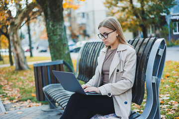 A business woman works with a laptop in Autumn Park. She has a great smile, long hair and big blue eyes. Portrait of a modern working woman. Yellow park background