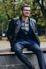 a young man in glasses sits on a bench