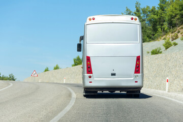 Big tourist bus rides along a mountain road with a protective wall.