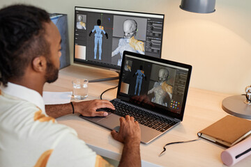 Back view at creative black man building digital 3D models and using multiple computer screens,...