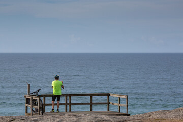 A cyclist with a phosphorescent green shirt looks at the sea from the wooden viewpoint of A Lanzada...