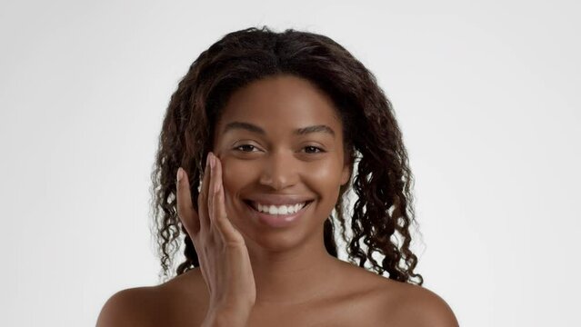 Seasonal facial care. Young african american woman applying protecting nourishing cream on cheek, white background