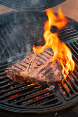 Barbecue dry aged wagyu porterhouse beef steak grilled as close-up on a charcoal grill with fire...