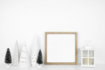 Christmas mock up with wooden frame, lantern and tree decor. Square frame on a white shelf against a white wall. Copy space.