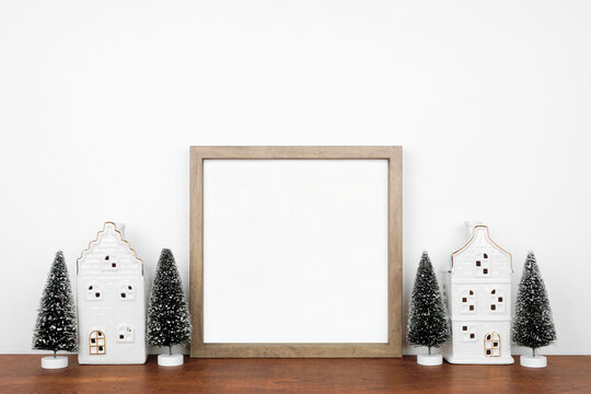 Christmas mock up with wooden frame, trees and white house decor. Square frame on a wood shelf against a white wall. Copy space.