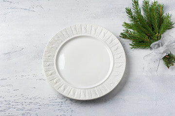 White ceramic plate with christmas tree branches decorated with silver ribbon on light gray...