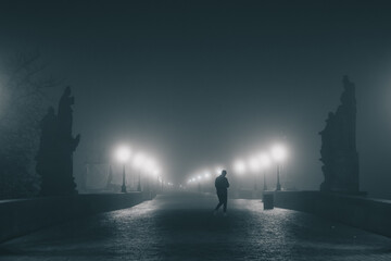 Charles or Karlov bridge in Prague in early morning hours with a lot of fog and haze, with visible...