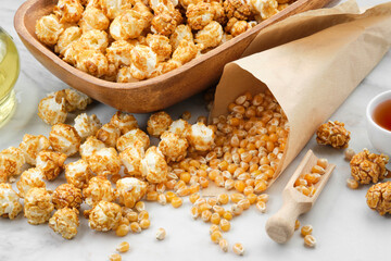 Popcorn in wooden bowl, corn grains, caramel sauce and oil bottle  on kitchen table.