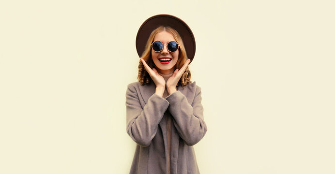 Portrait of beautiful smiling young woman model wearing brown round hat and coat on beige background