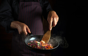 The cook prepares fresh vegetables in a frying pan. advertising space on a dark background. Hotel vegetarian recipe idea