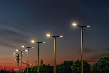 A modern street LED lighting pole. Urban electro-energy technologies. A row of street lights against the night sky - obrazy, fototapety, plakaty