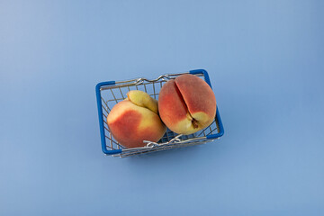 Two Deformed peaches in shopping basket on blue background, selective focus, copy space. Ugly...