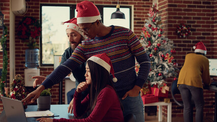 Diverse coworkers working on startup report in festive office, doing teamwork at desk during...