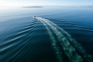 Small ferry boat in blue ocean on the way to Aran island, Ireland. Wake behind cruise ship. Warm...