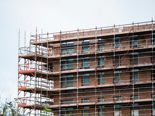 Fototapeta na wymiar Construction site with modern building in scaffolding. Brick house, residential or commercial property development.