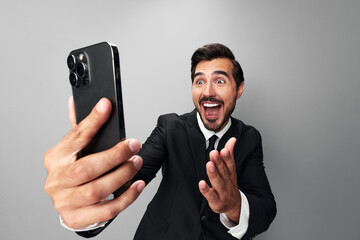Man businessman holding phone in hand surprised looking at screen video call and selfies and smile...