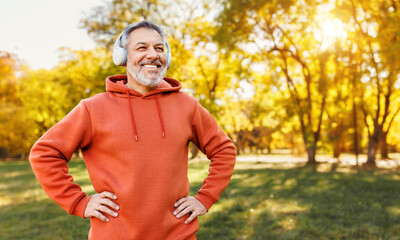 Happy positive mature man with broad in headphones  smile  while doing sport in city park - obrazy, fototapety, plakaty