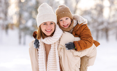Mom giving piggyback ride to happy little son while walking outdoors in snowy winter park