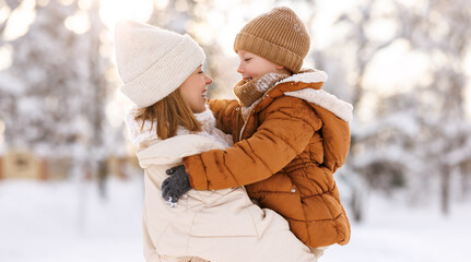 Happy family enjoying snowy weather outdoor, mom with little son hugging during walk in winter park
