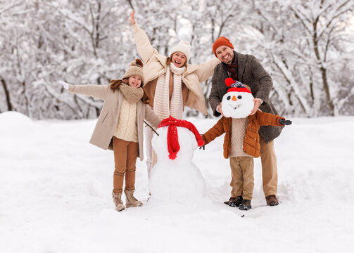 Happy father, mother and kids having fun outdoor while making snowman together in winter snowy park